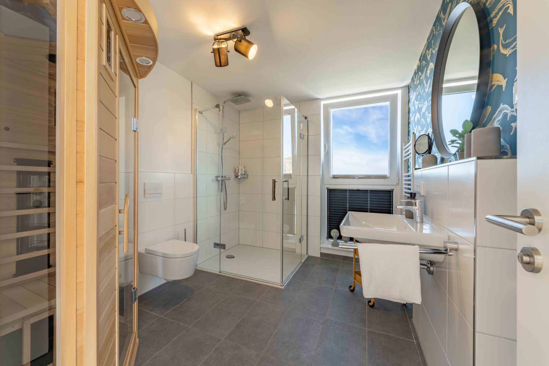 Modernes Badezimmer mit Sauna, großer Dusche, Wandtoilette, Waschbecken und Fenster.