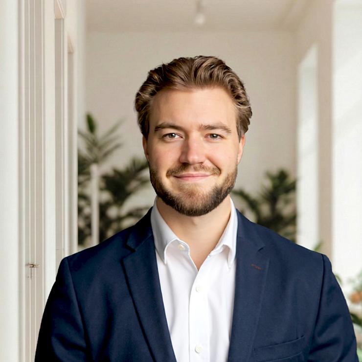 Ein Mann im Anzug steht in einem hellen Raum mit großen Fenstern und Pflanzen.