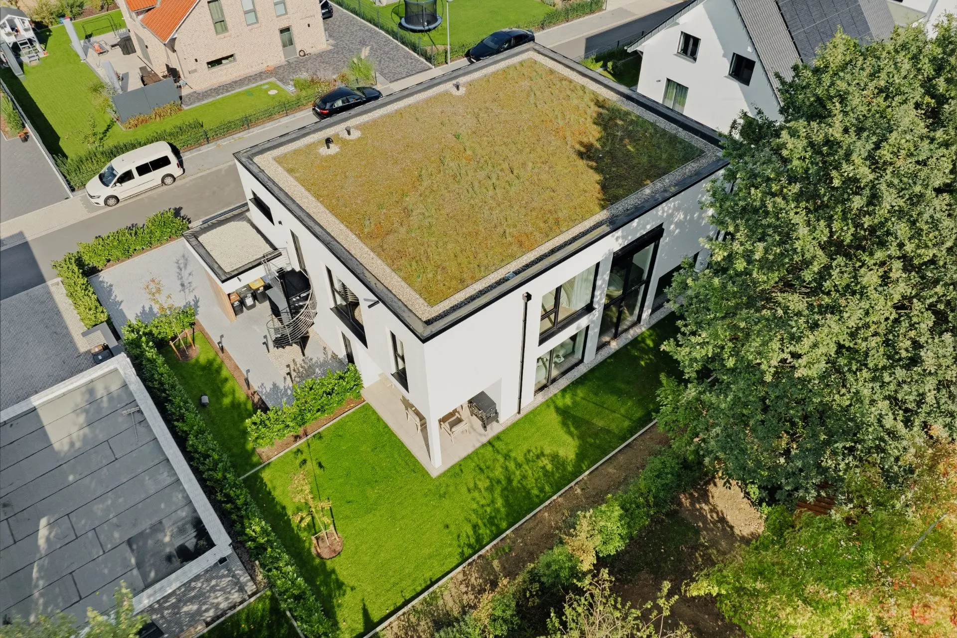 Modernes Wohnhaus mit Flachdach und begrüntem Dach, umgeben von Garten und Terrasse.