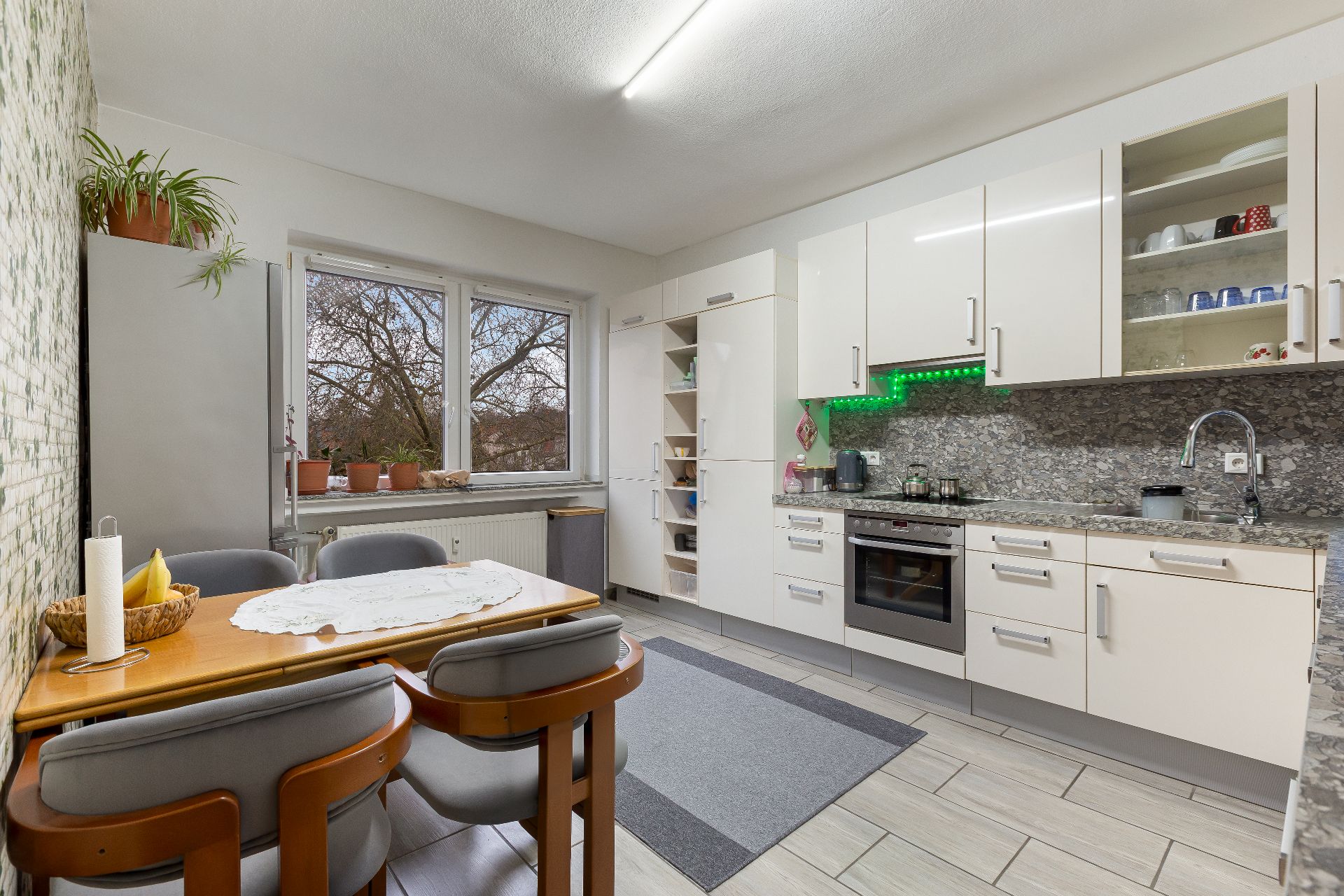 Moderne Küche mit Esstisch, vier Stühlen, weißen Schränken und Fenster mit Pflanzen.