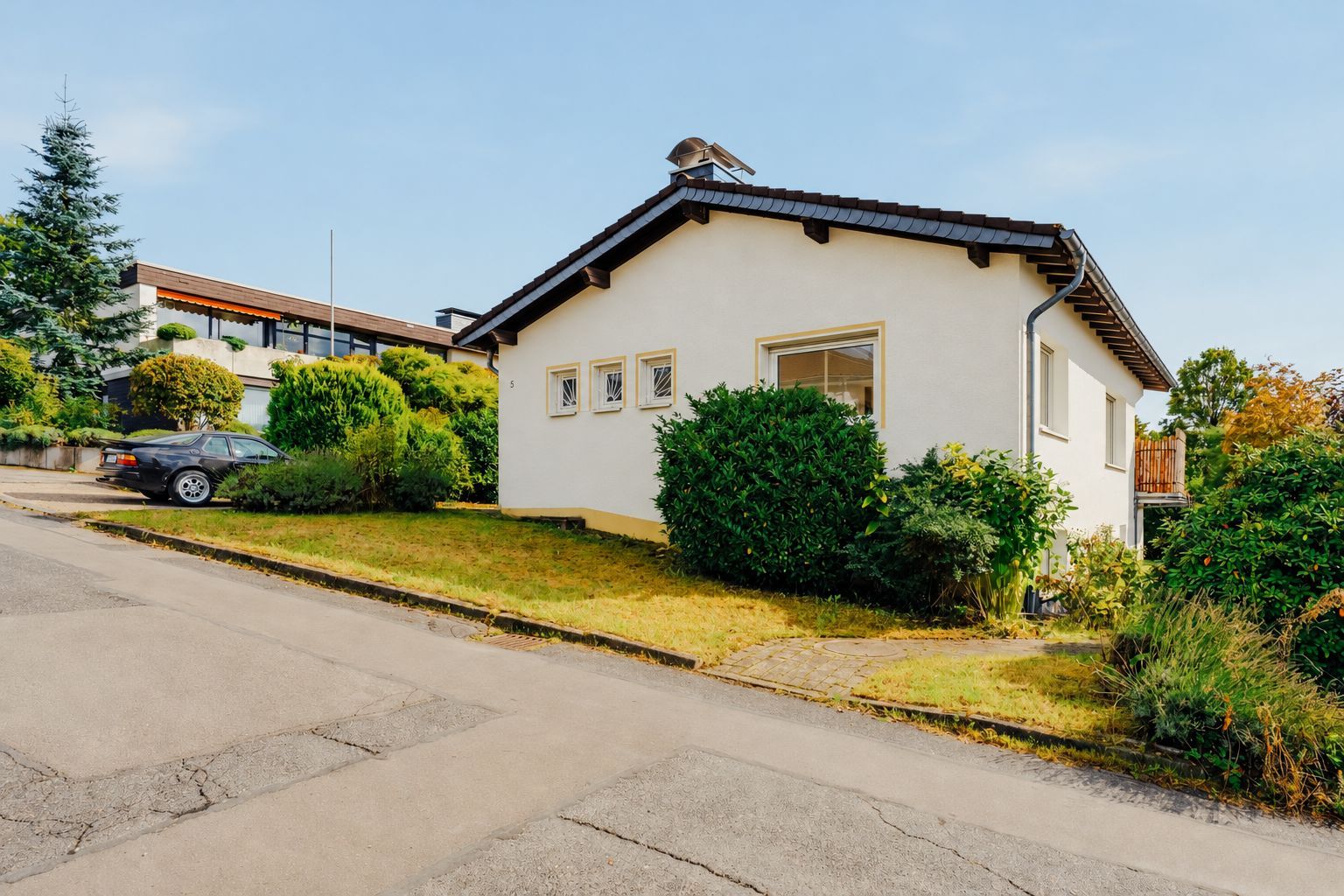 Einfamilienhaus mit hellem Putz, dunklem Dach und gepflegtem Garten an einer ruhigen Straße.