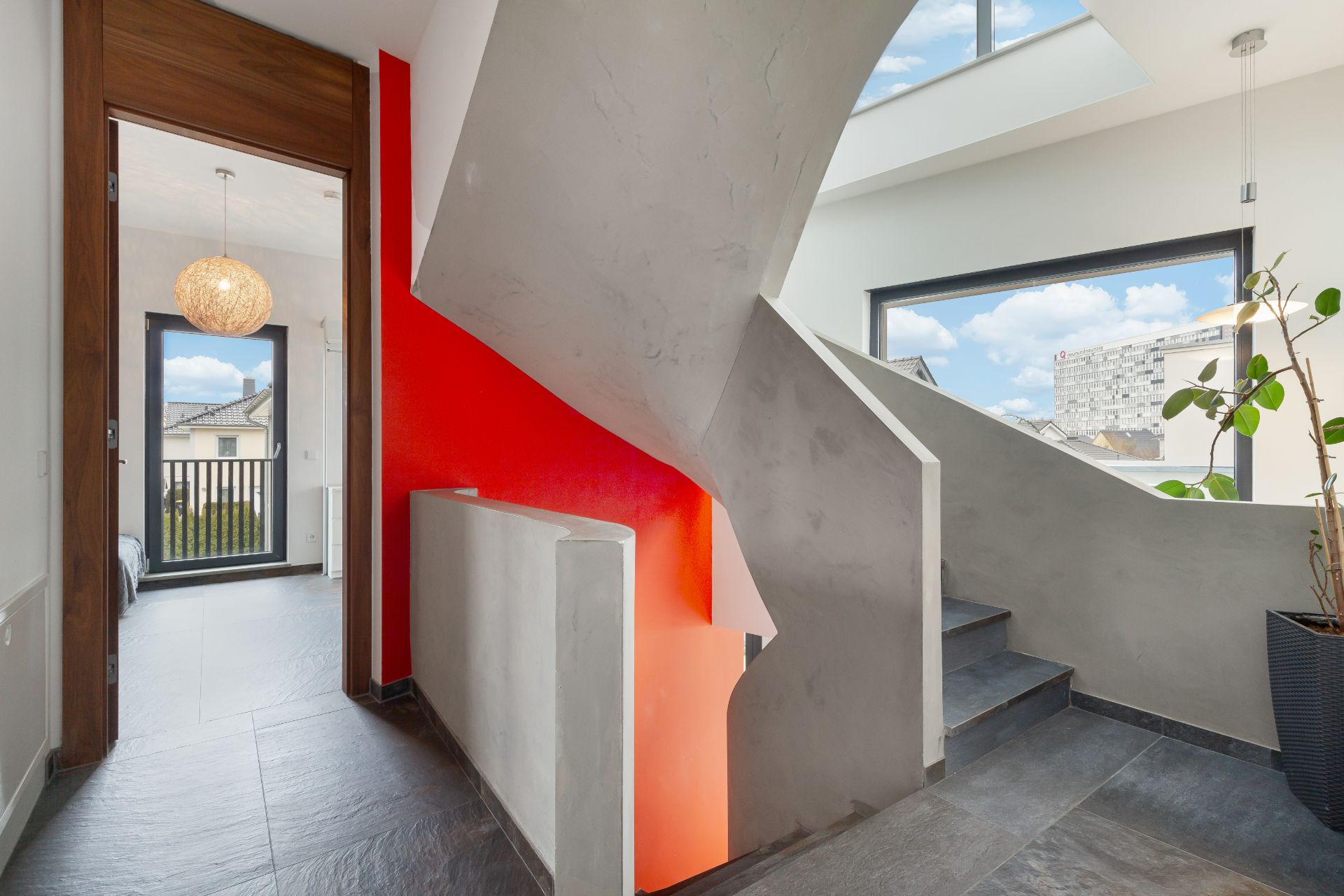 Moderne Treppe mit grauem Geländer und roter Wand, große Fenster mit Ausblick.