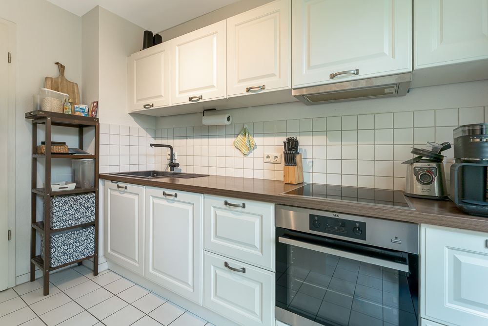 Helle Küche mit weißen Schränken, Herd, Spüle und Regal an der linken Wand.