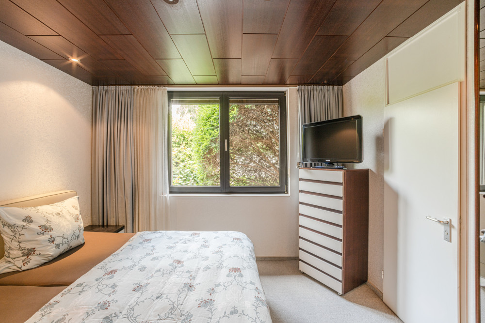 Schlafzimmer mit Doppelbett, Fenster, Kommode und Fernseher.
