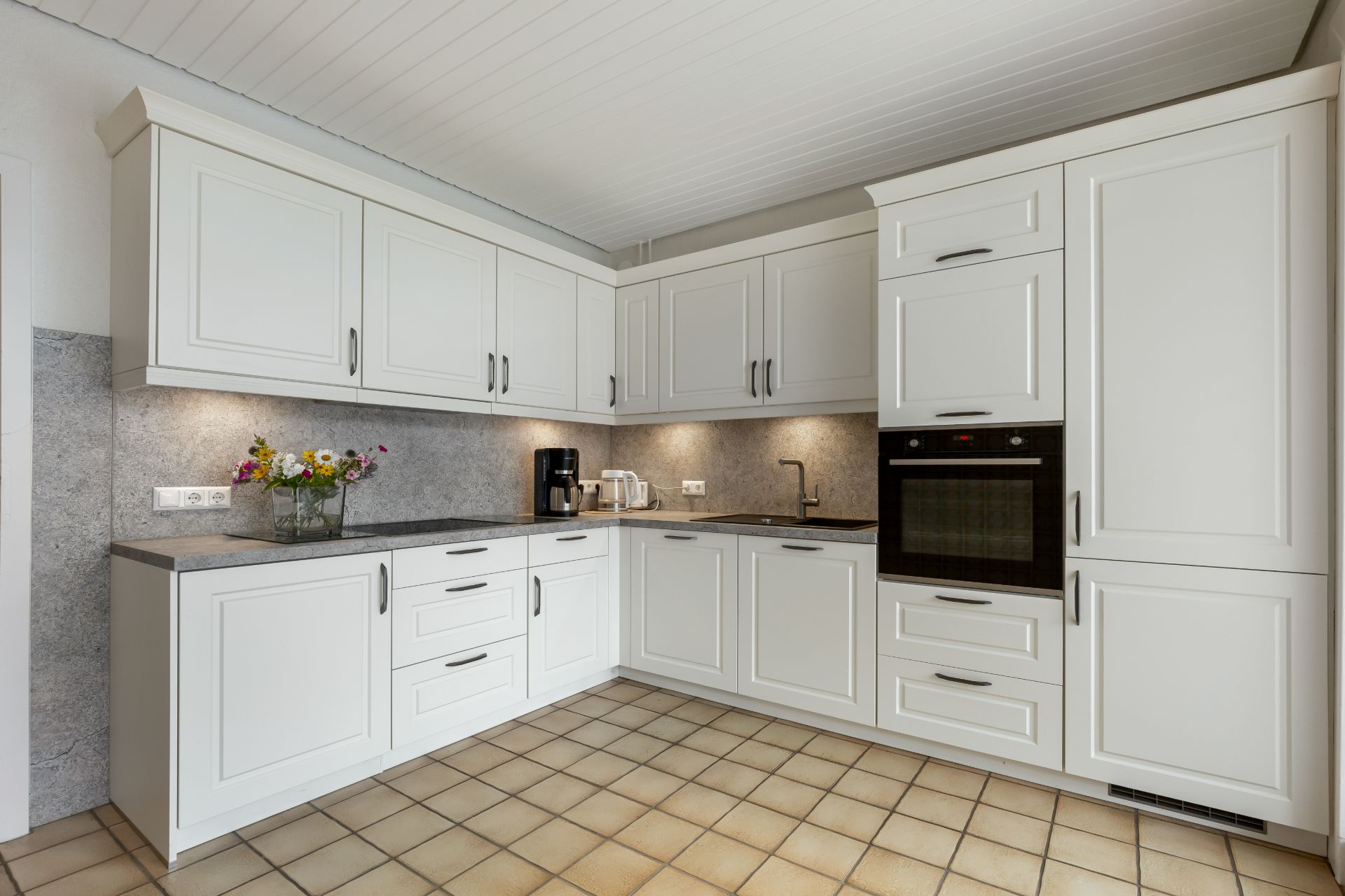 Moderne Einbauküche mit weißen Schränken, Backofen und Arbeitsfläche mit Küchengeräten.