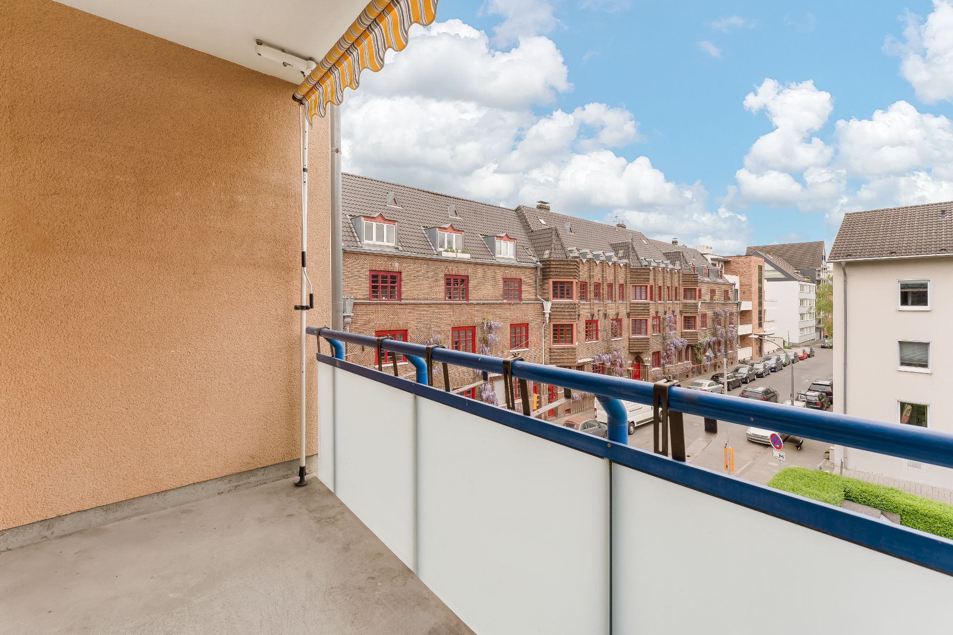 Balkon mit Markise und Blick auf eine ruhige Wohnstraße und Backsteinhäuser.