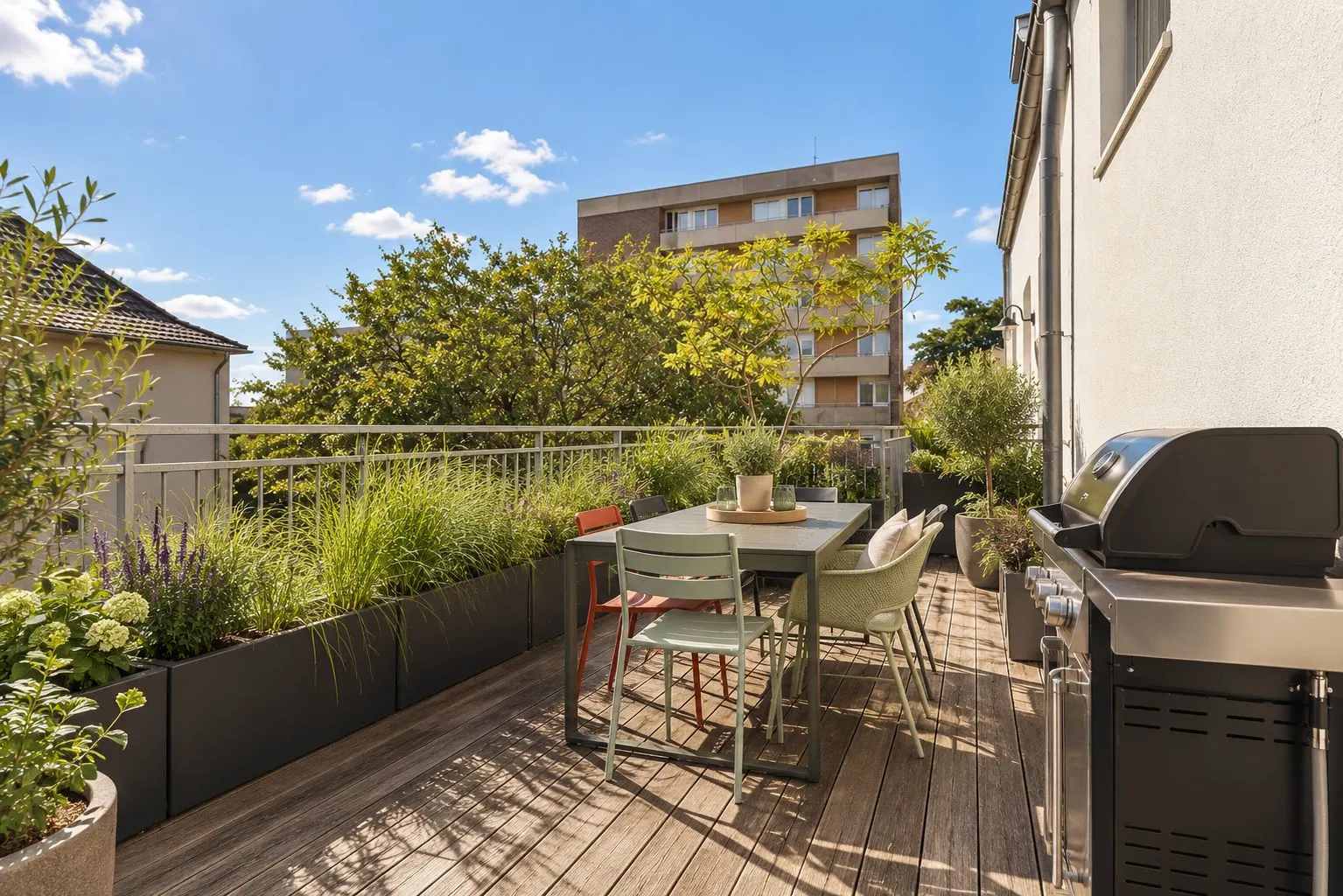 Sonnige Terrasse mit Holzboden, Esstisch, Stühlen, Grill und vielen Pflanzen.