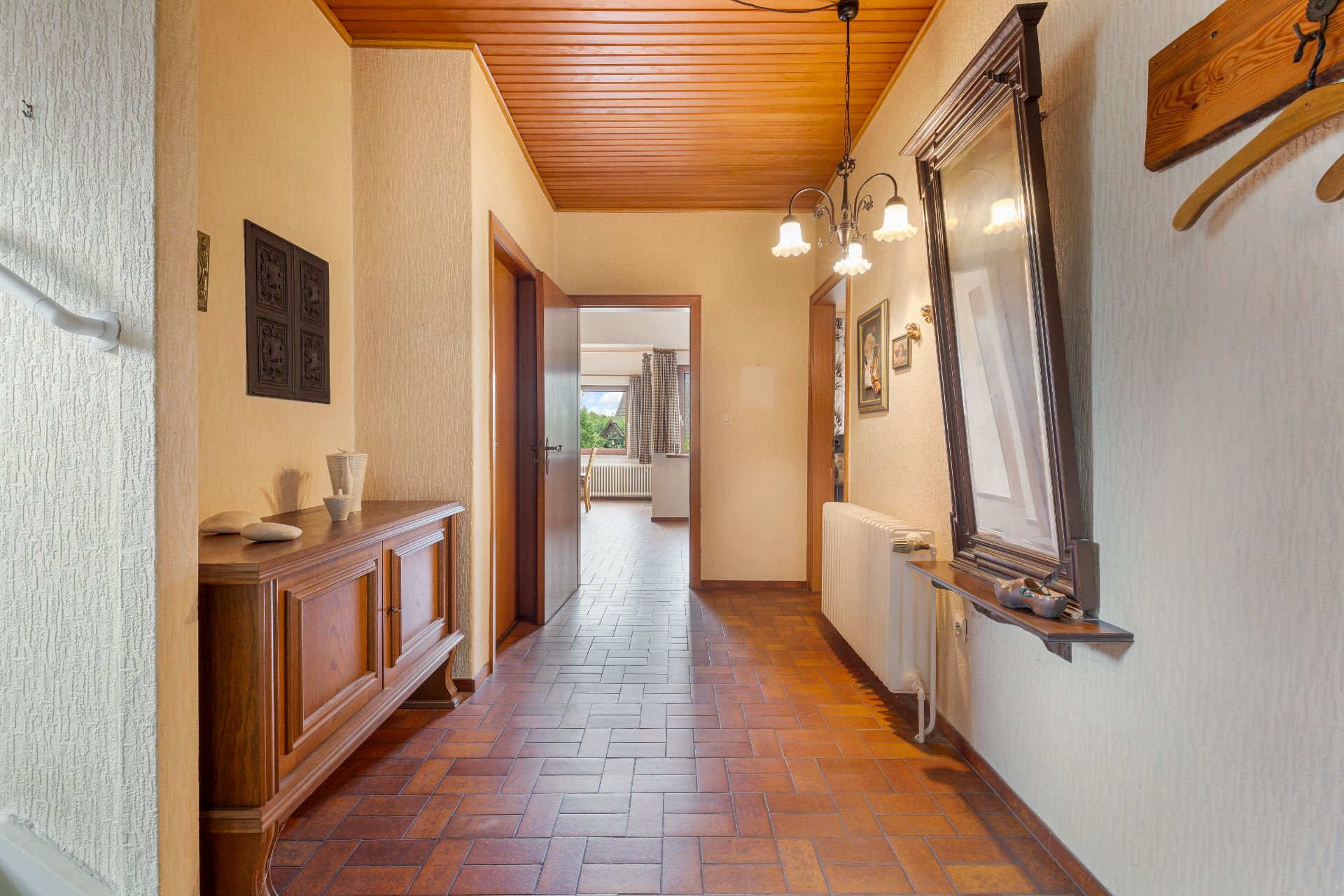 Heller Flur mit braunem Fliesenboden, Holzdecke und seitlichem Fenster in einem Wohnhaus.