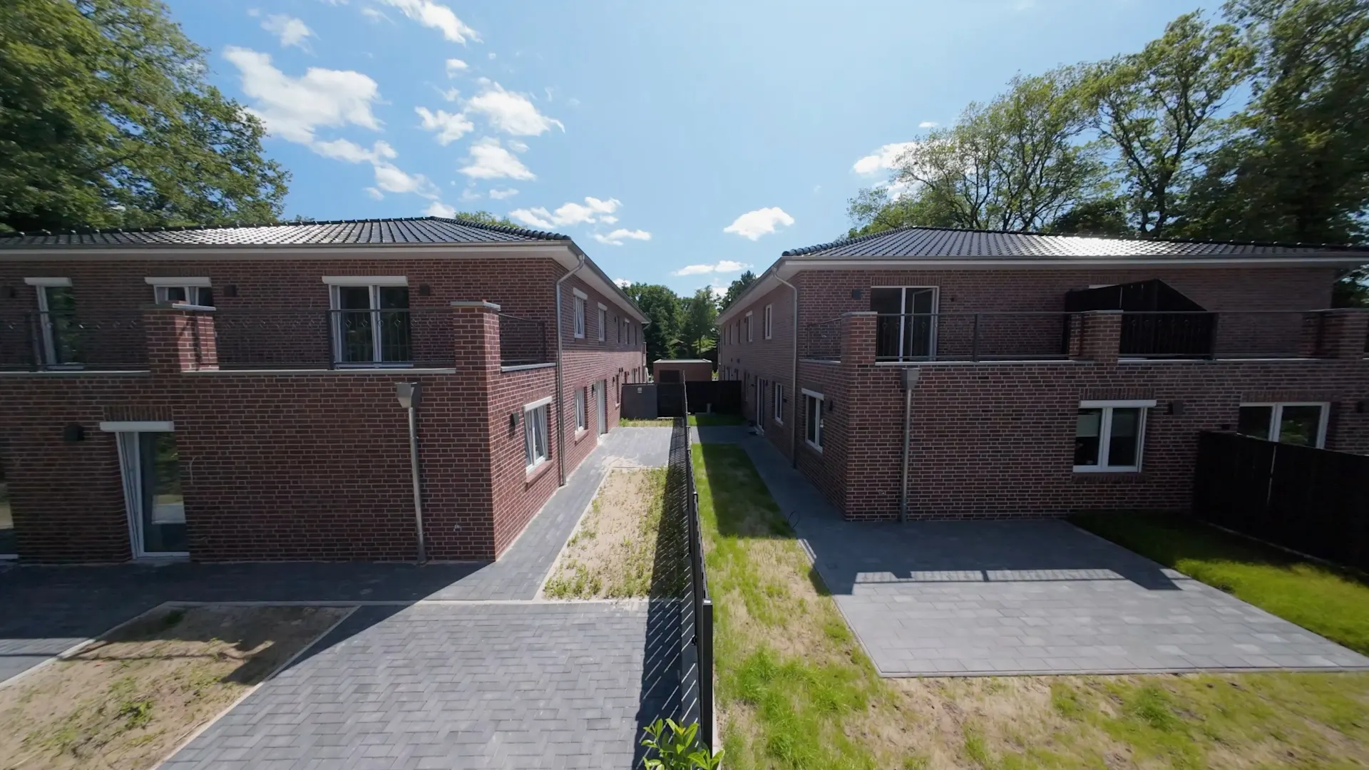 Zwei moderne, zweistöckige Backsteinhäuser mit gepflasterten Wegen und kleinem Gartenbereich.