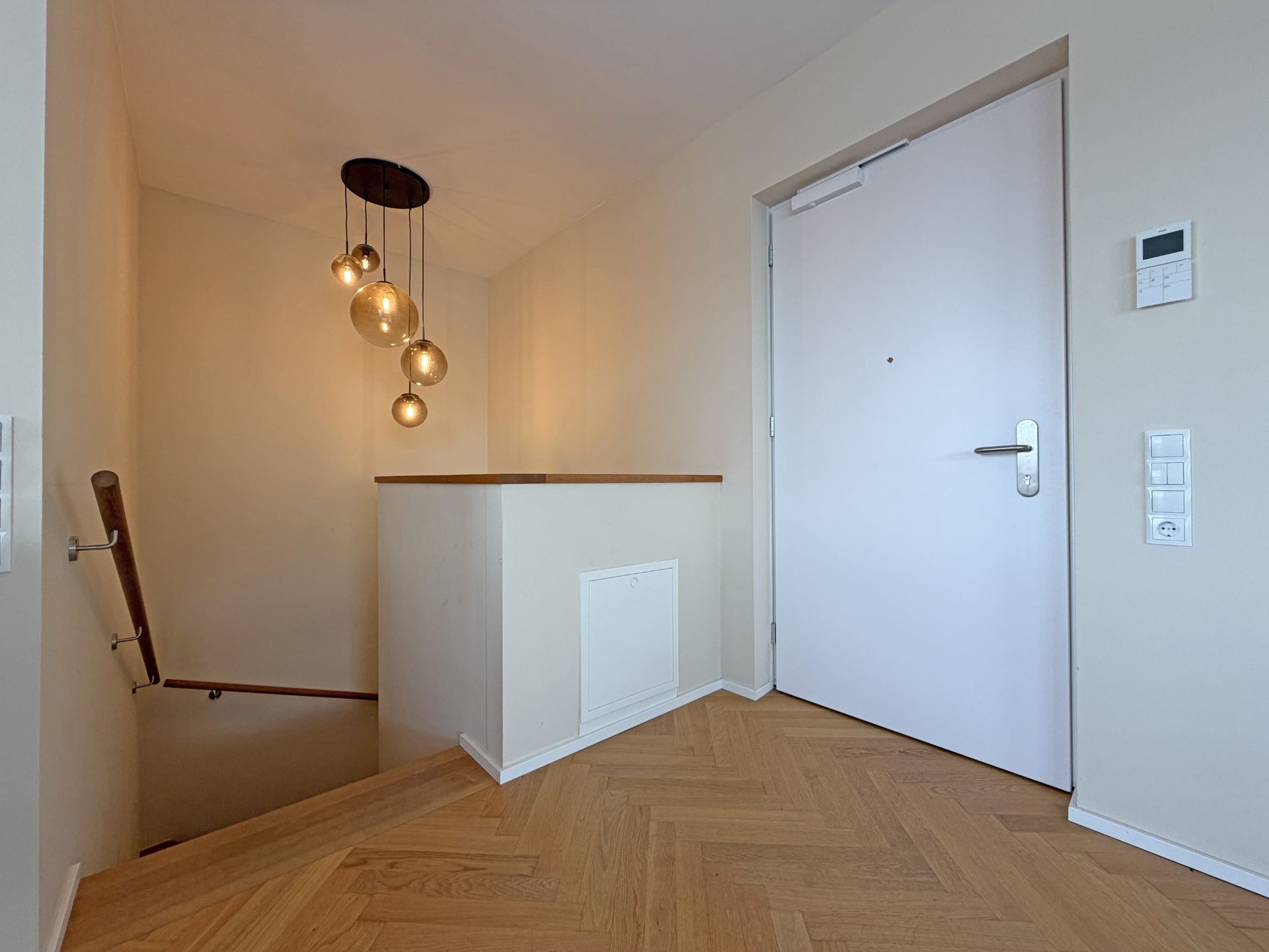 Heller Flur mit weißer Eingangstür, Treppe nach unten und modernen Deckenleuchten.