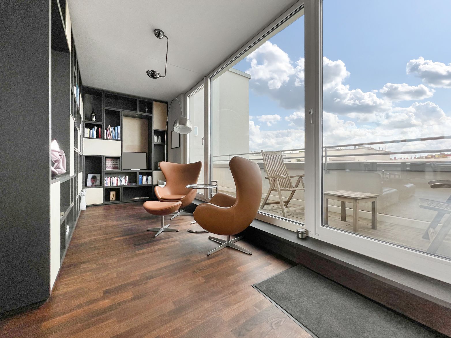 Wohnzimmer mit zwei braunen Sesseln, Bücherregal und großer Fensterfront zur Terrasse.