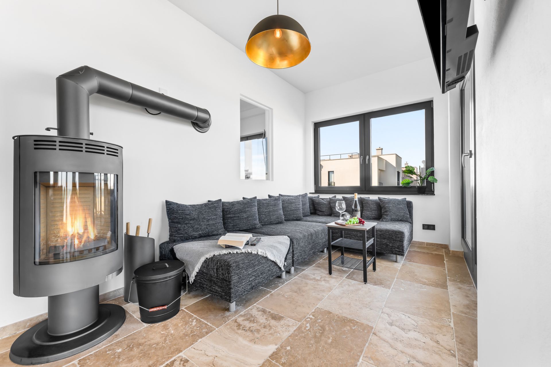 Helles Wohnzimmer mit Kamin, Ecksofa, Couchtisch und großen Fenstern.