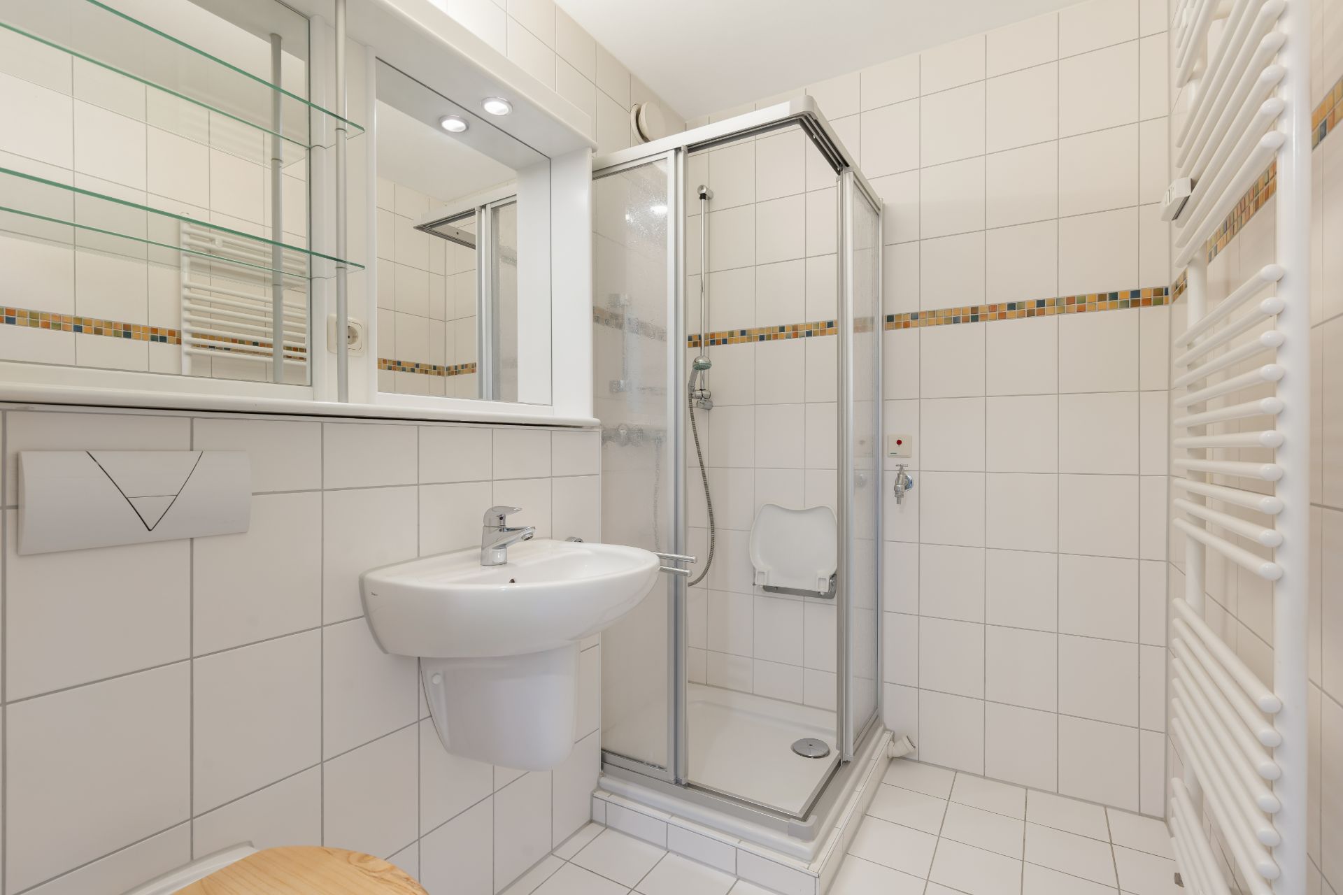 Modernes Badezimmer mit Dusche, Waschbecken, Spiegel und Handtuchheizkörper, weiß gefliest.