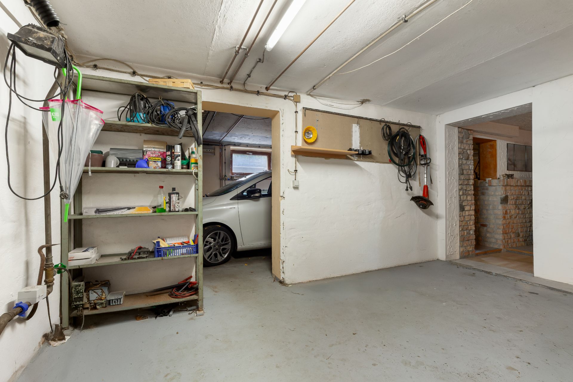Garage mit Regal voller Werkzeuge und einem Auto, das halb sichtbar ist.