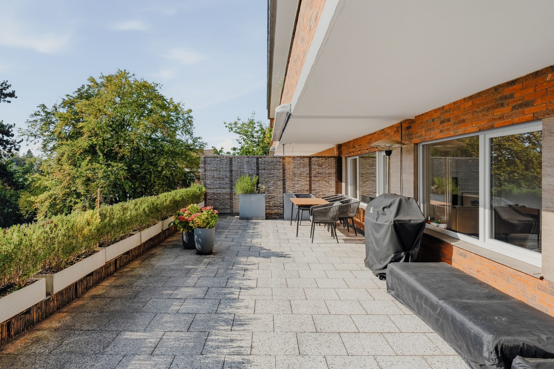 Große Terrasse mit Sitzbereich, Pflanzenkübeln und Blick auf Bäume.