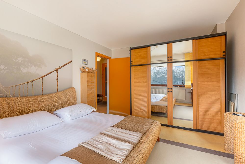 Helles Schlafzimmer mit Bett, Rattanmöbeln und großem Kleiderschrank mit Spiegel.