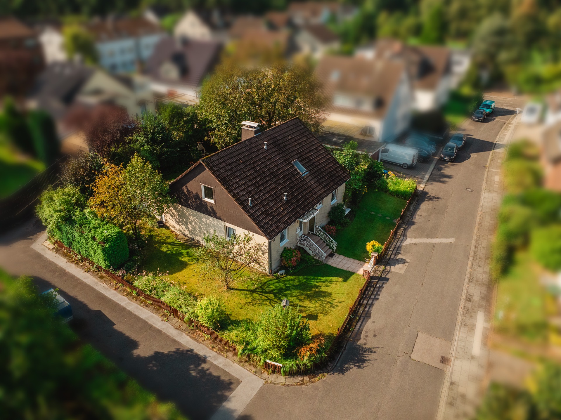 Einfamilienhaus mit Garten an einer Straßenecke, umgeben von Bäumen und Sträuchern.