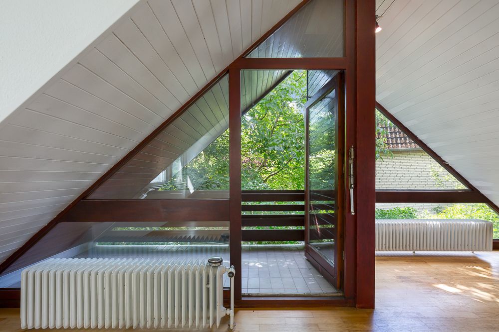 Dachzimmer mit schräger Decke, großer Glasfront und Zugang zu einem Balkon.