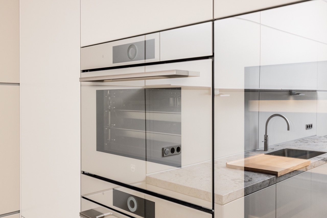 Moderne Einbauküche mit Backofen, Spüle, Wasserhahn und Schneidebrett auf der Arbeitsplatte.