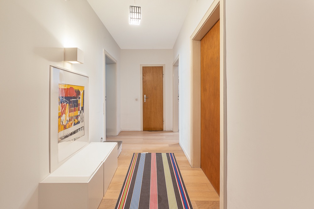 Heller Flur mit Holzboden, buntem Teppich, Bild an der Wand und mehreren Türen.