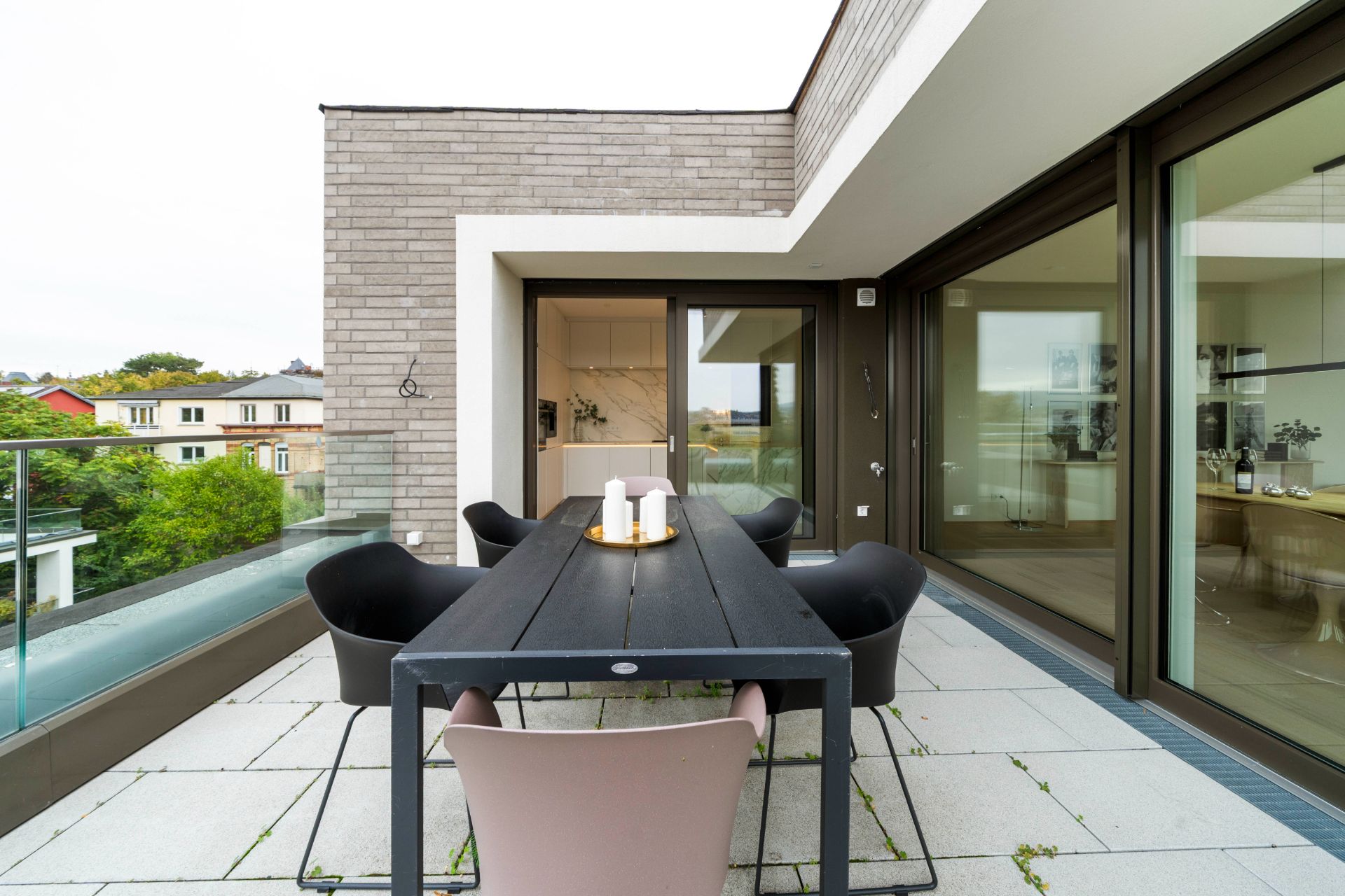 Moderne Terrasse mit Esstisch, Stühlen und Glasgeländer vor Wohnhaus.
