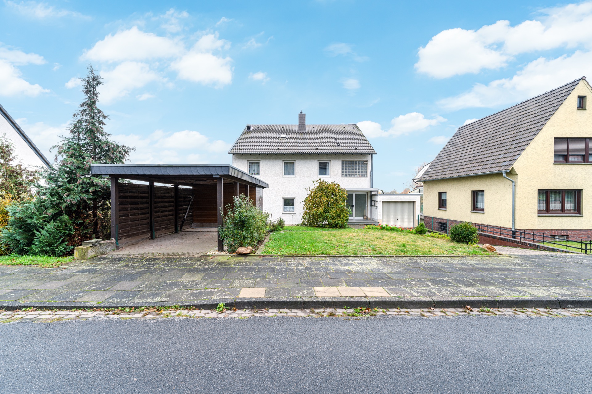 Zweistöckiges Wohnhaus mit Carport, Garage und Vorgarten, daneben ein weiteres Haus.