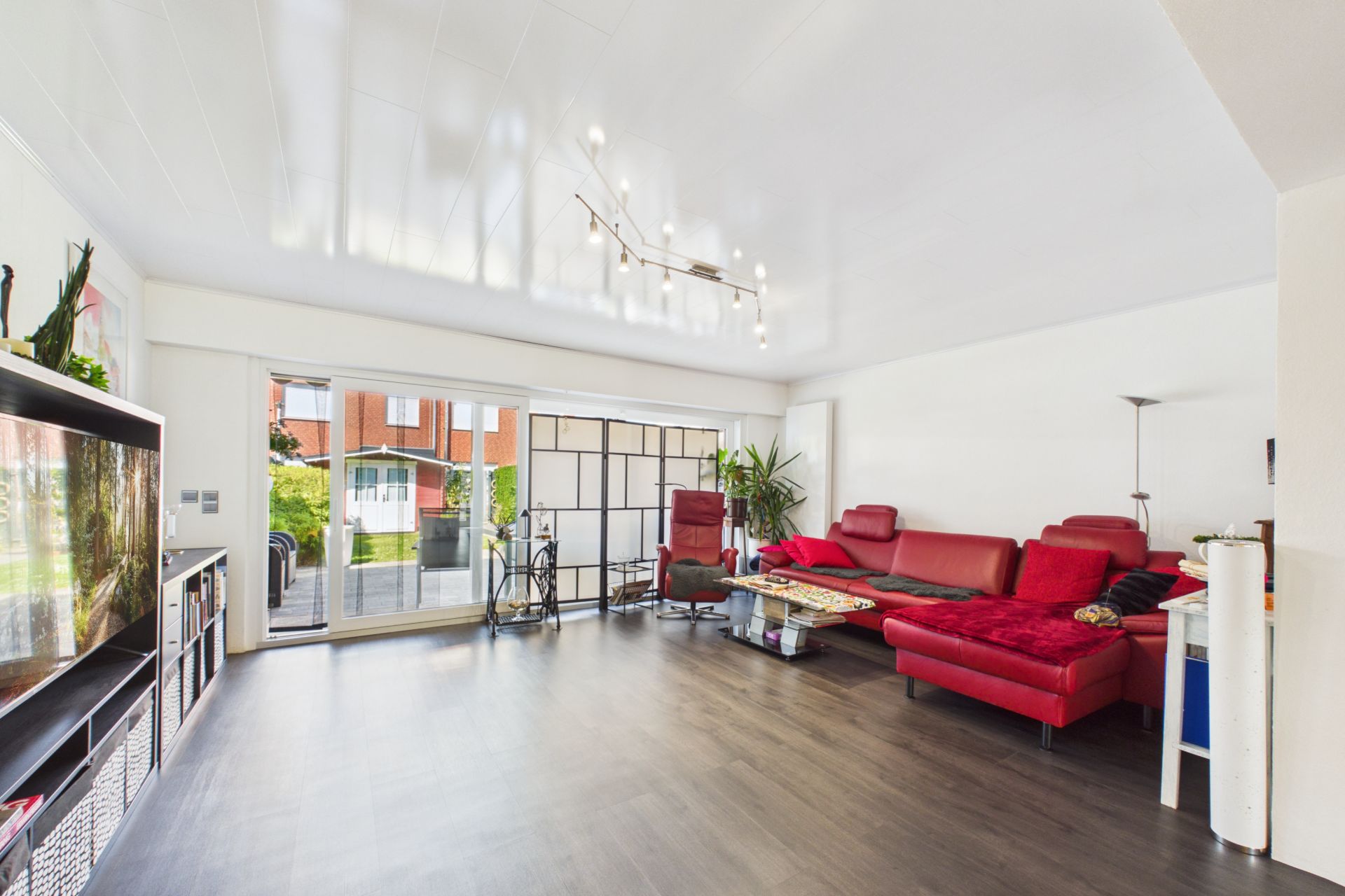 Modernes Wohnzimmer mit rotem Sofa, Glastüren zum Garten und dunklem Holzboden.