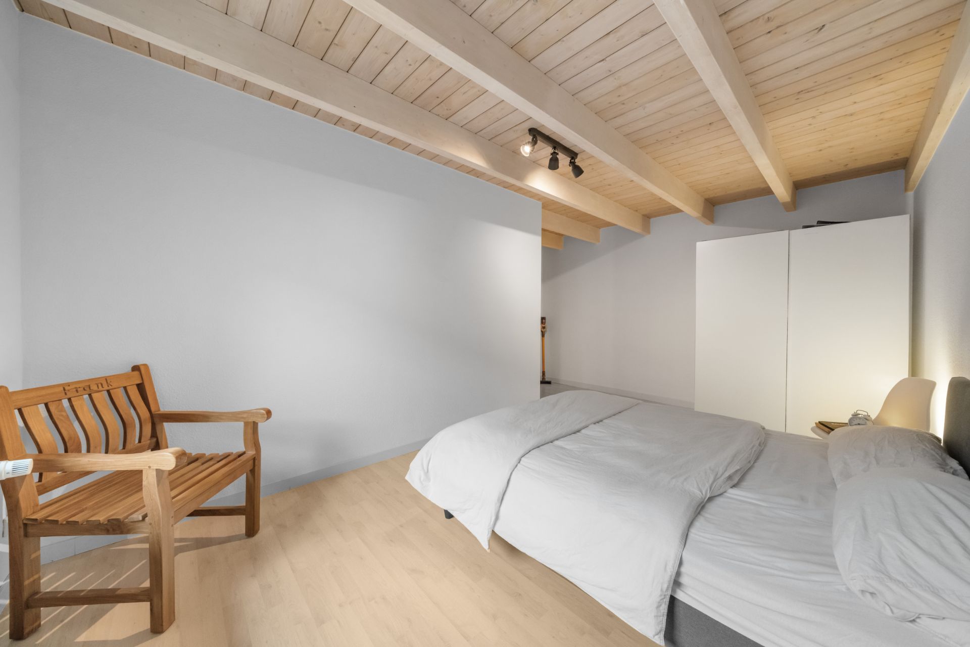 Schlafzimmer mit Holzbett, weißem Kleiderschrank und Holzbalkendecke.