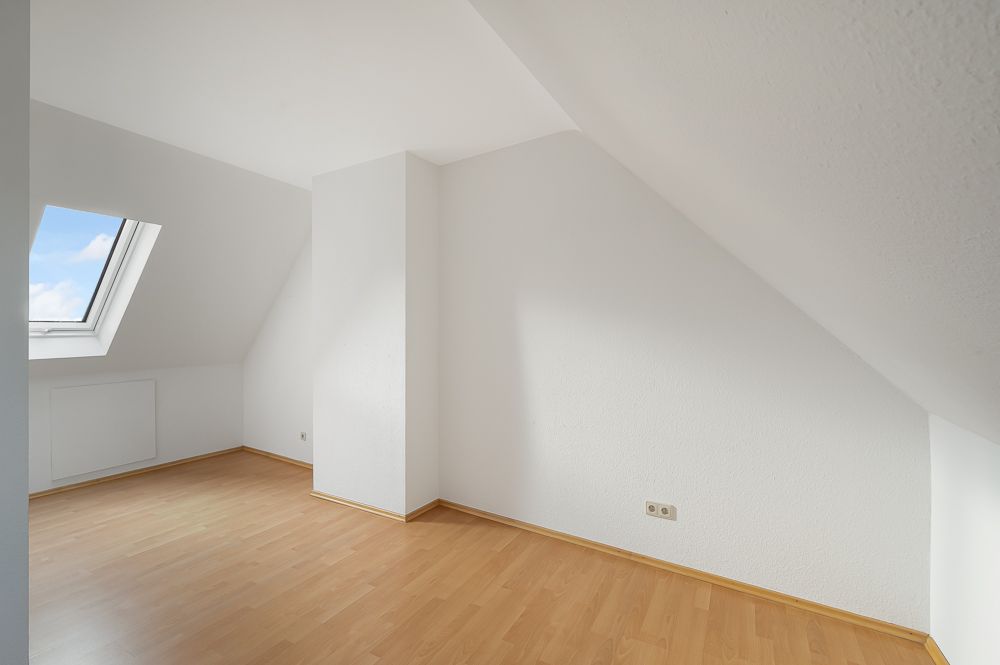 Heller Raum mit Dachschräge, weißer Wand, Laminatboden und Dachfenster.
