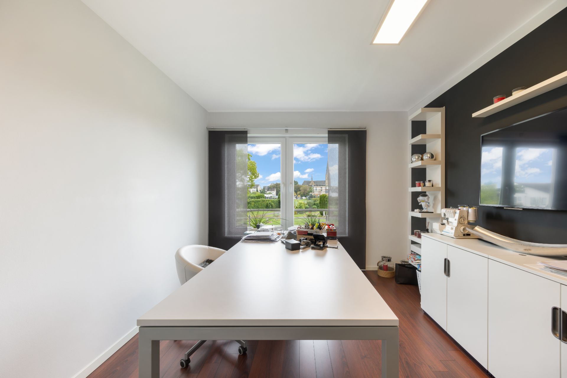 Modernes Arbeitszimmer mit Schreibtisch, Stuhl, Regalen und großem Fenster mit Blick nach draußen.