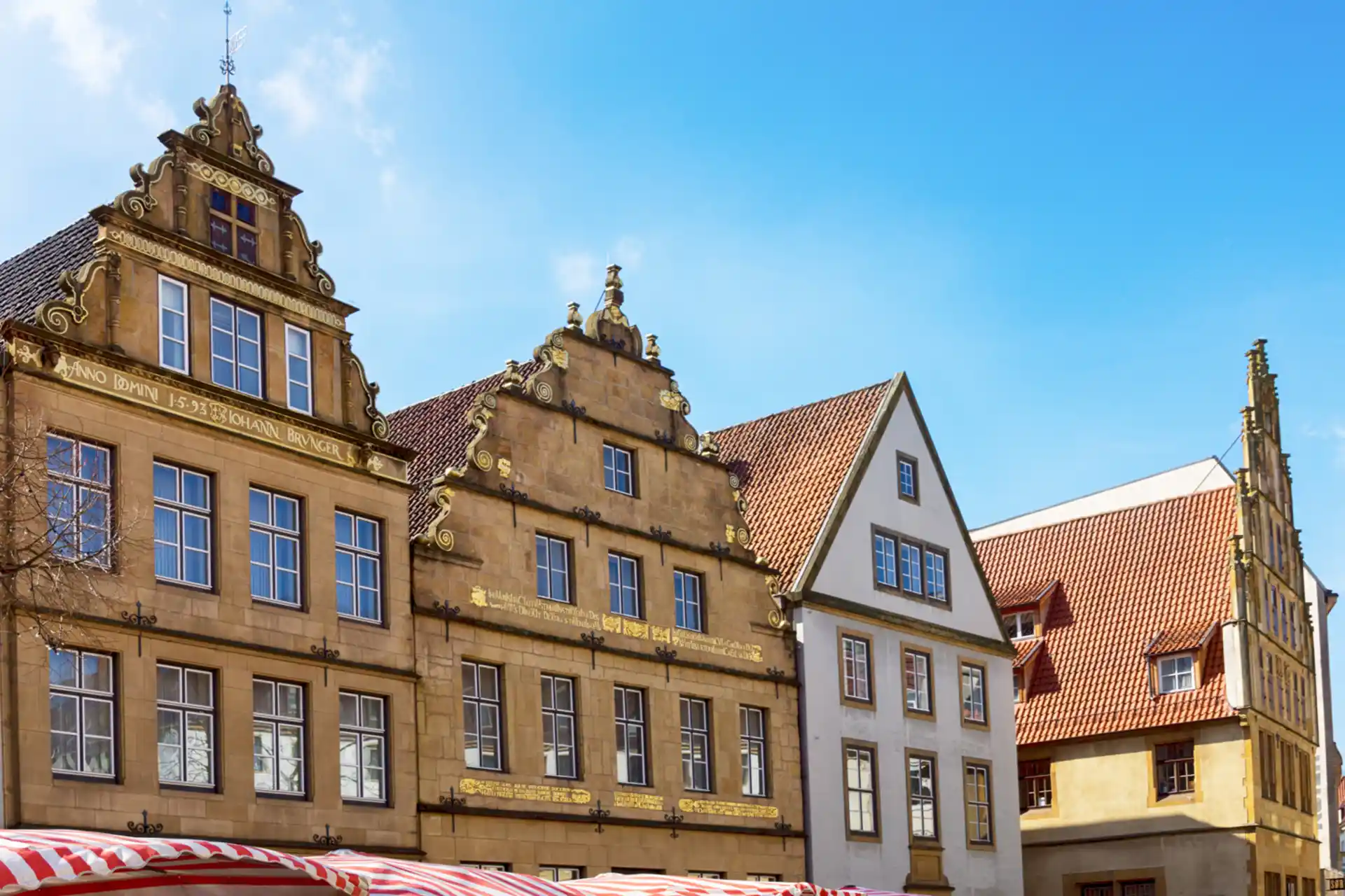 Historische Wohnhäuser mit verzierten Giebeln und roten Dachziegeln bei blauem Himmel.
