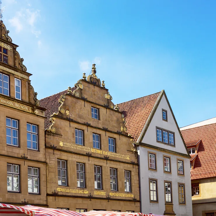 Historische Wohnhäuser mit verzierten Giebeln und roten Dachziegeln bei blauem Himmel.