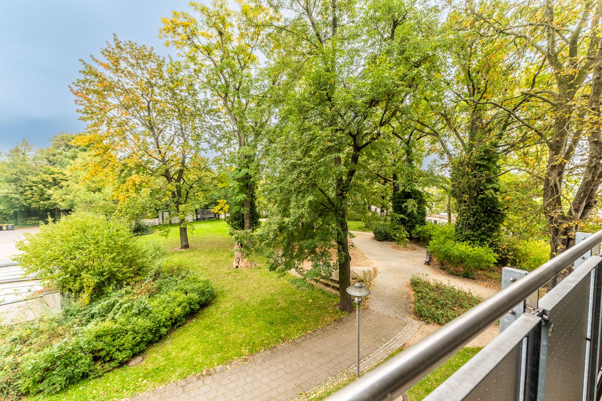Blick von einem Balkon auf einen grünen Park mit Bäumen und Gehwegen.