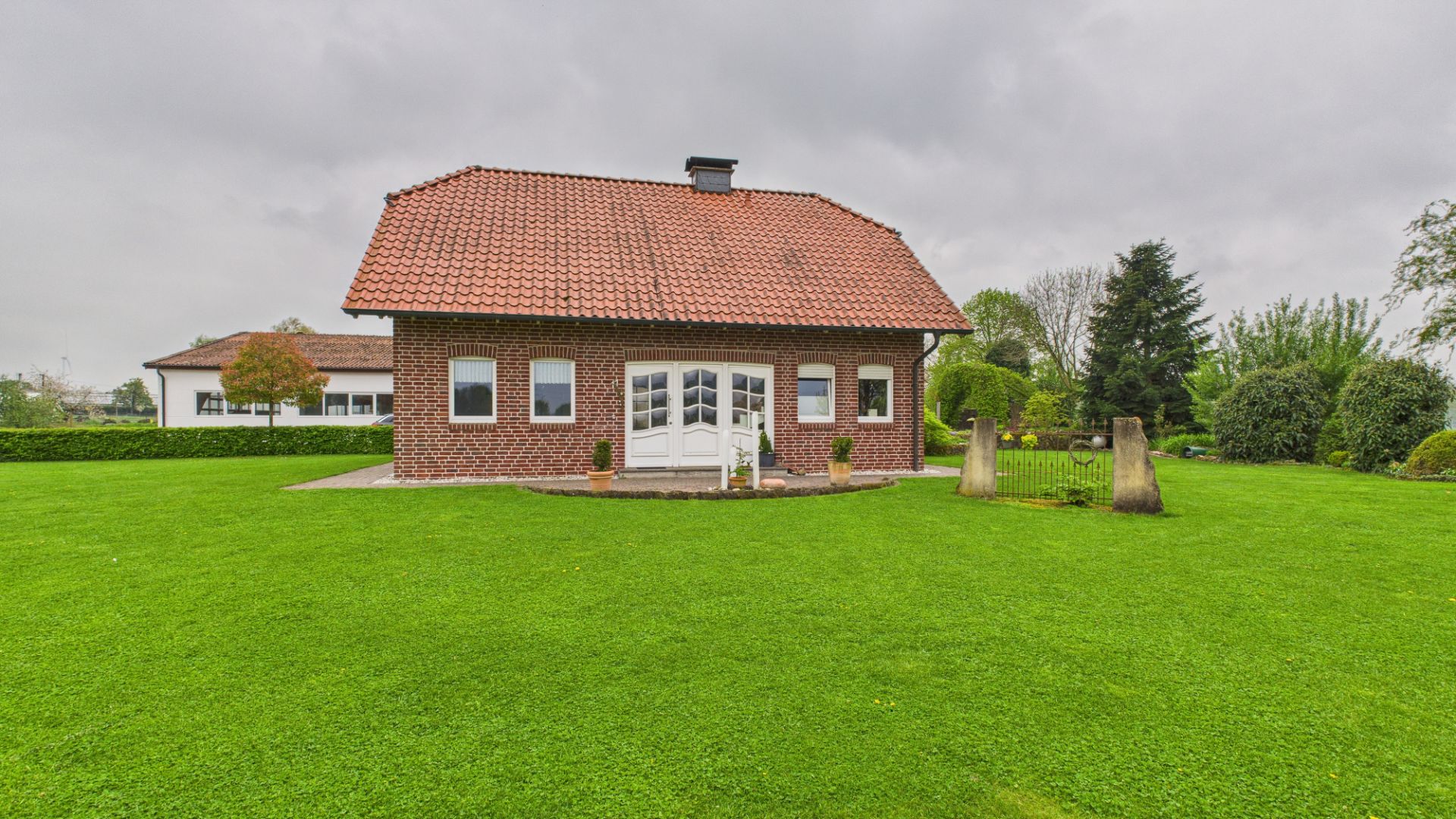 Backsteinwohnhaus mit rotem Dach und großem grünen Garten, aufgenommen von vorne.
