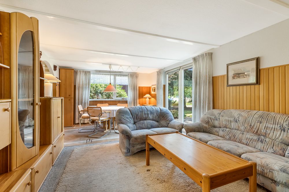 Wohnzimmer mit zwei Sofas, Holztisch, Schrankwand und Blick auf Garten durch große Fenster.