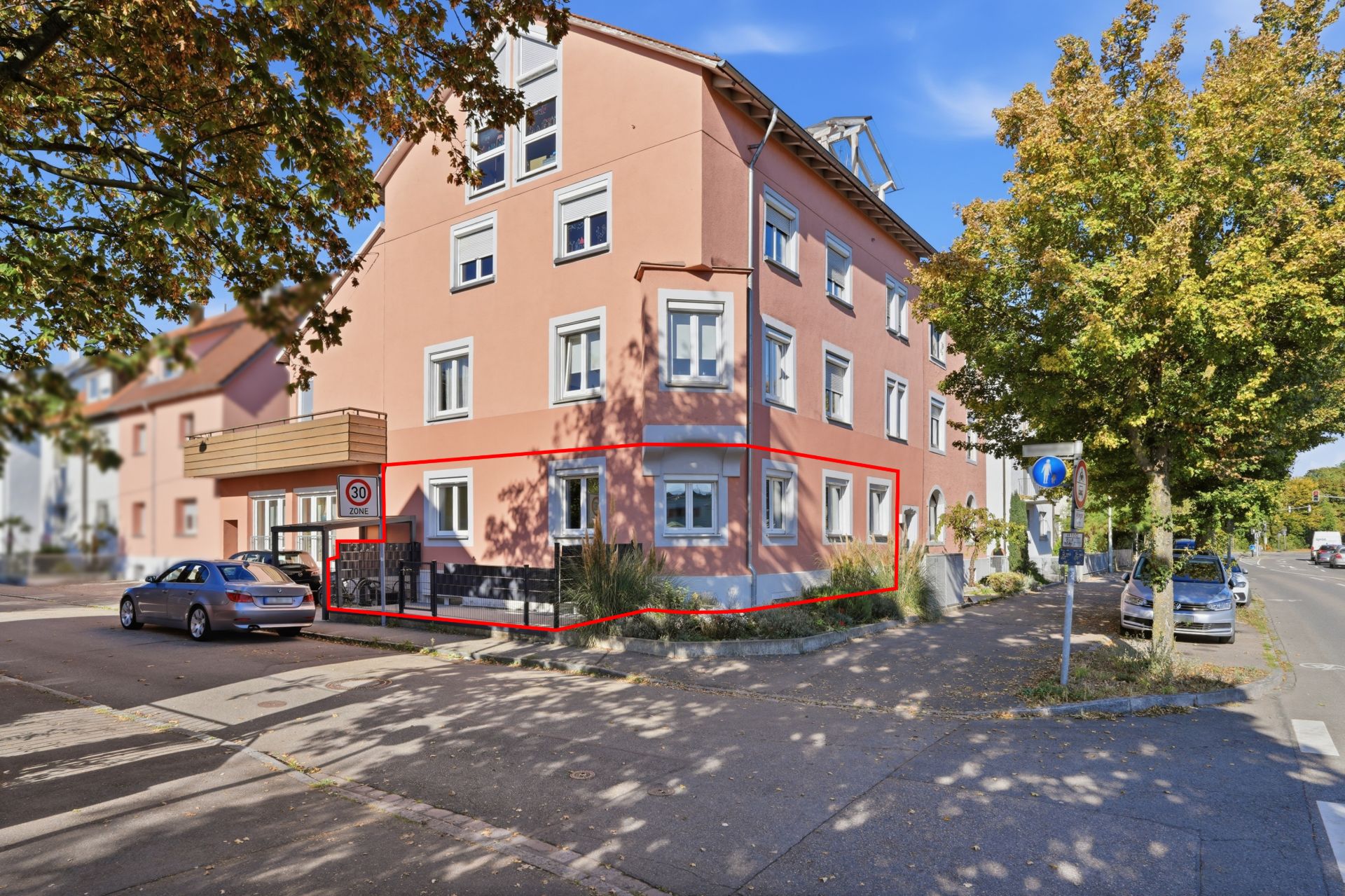 Rosa Wohnhaus an einer Straßenecke mit markiertem Bereich im Erdgeschoss und geparkten Autos.