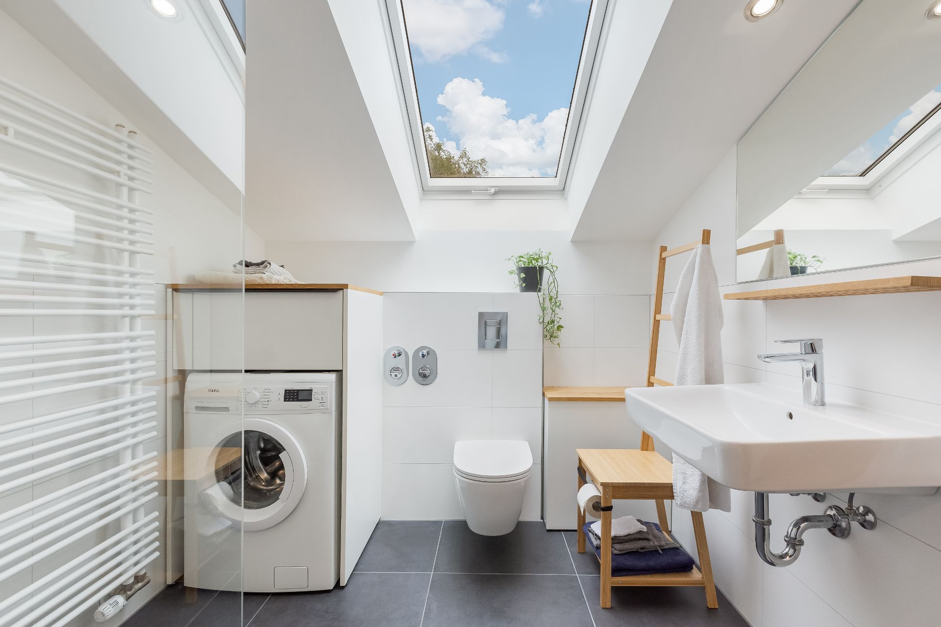 Modernes Bad mit Dachfenstern, Waschmaschine, WC, Waschbecken und Handtuchleiter.