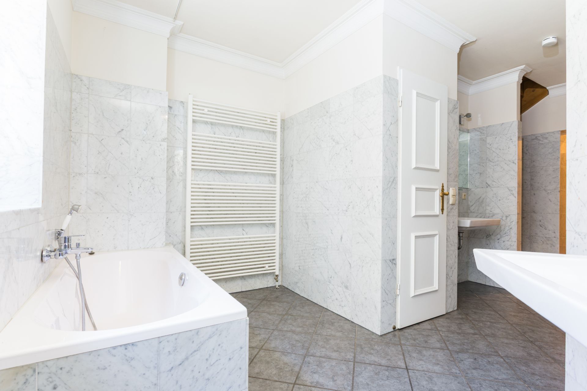 Modernes Badezimmer mit Badewanne, Waschbecken, Handtuchheizkörper und grauen Fliesen.