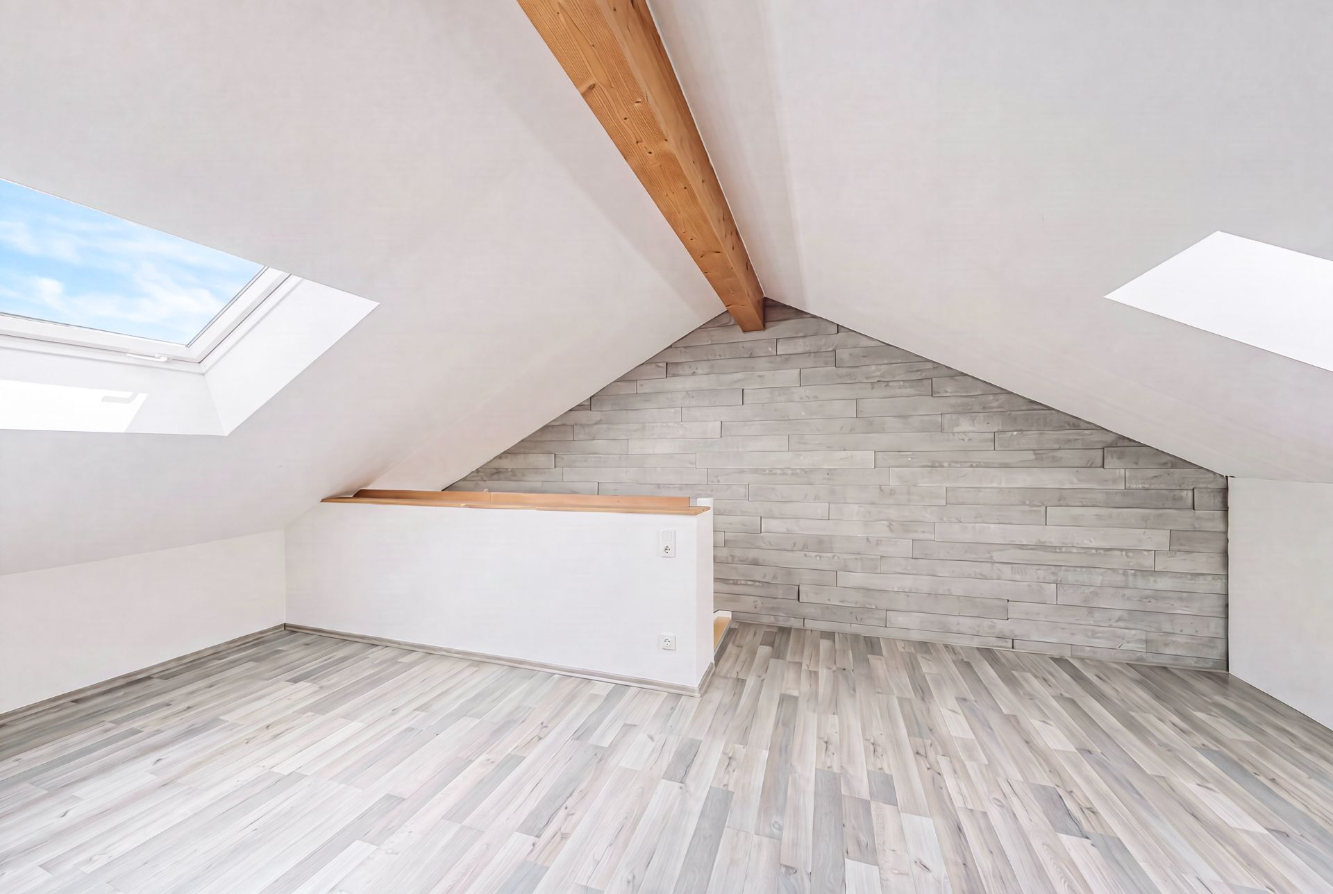 Heller Dachgeschossraum mit schrägen Decken, Holzträger und zwei Dachfenstern.