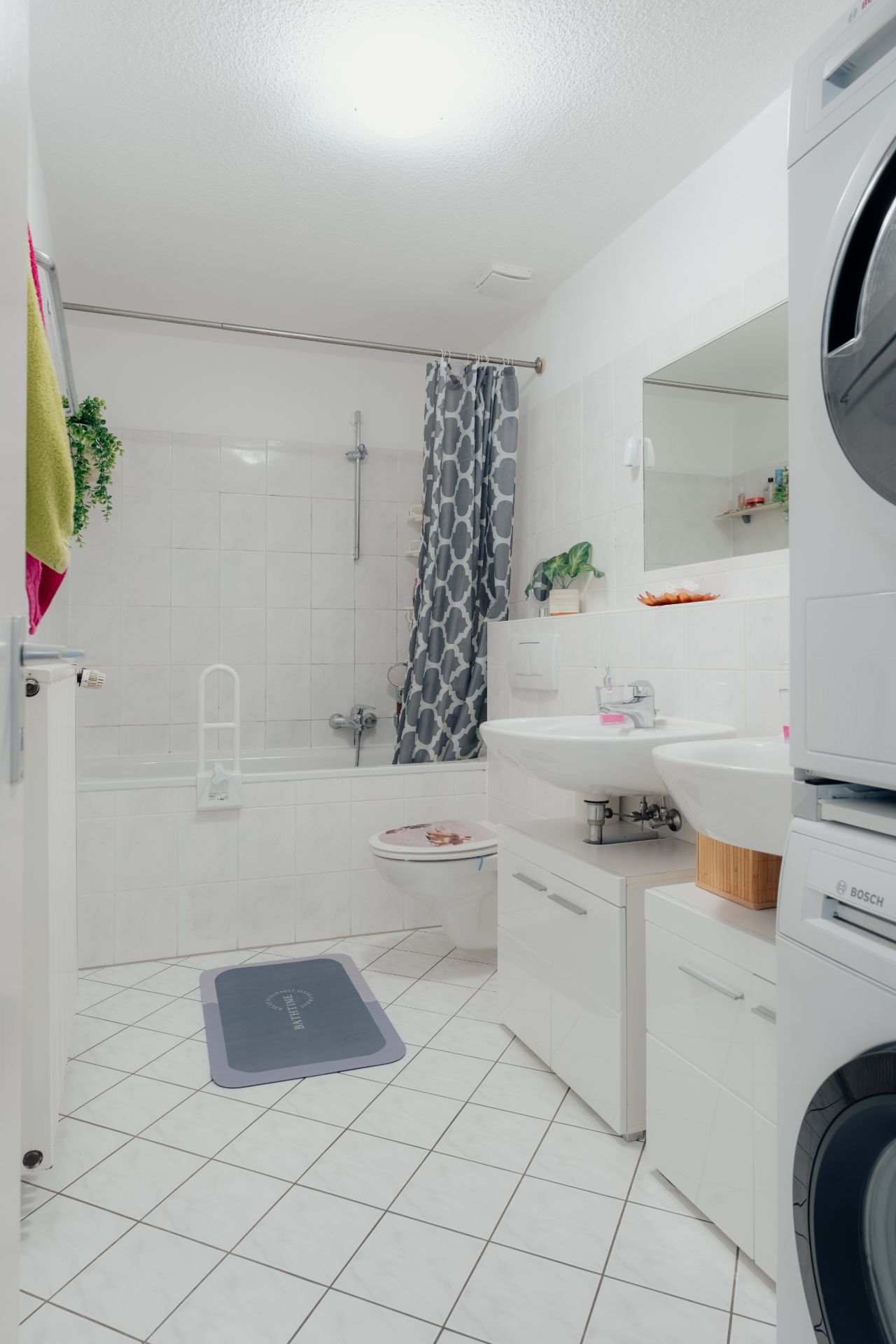 Helles Badezimmer mit Fliesen, Badewanne, Waschbecken, Toilette und Waschmaschine.