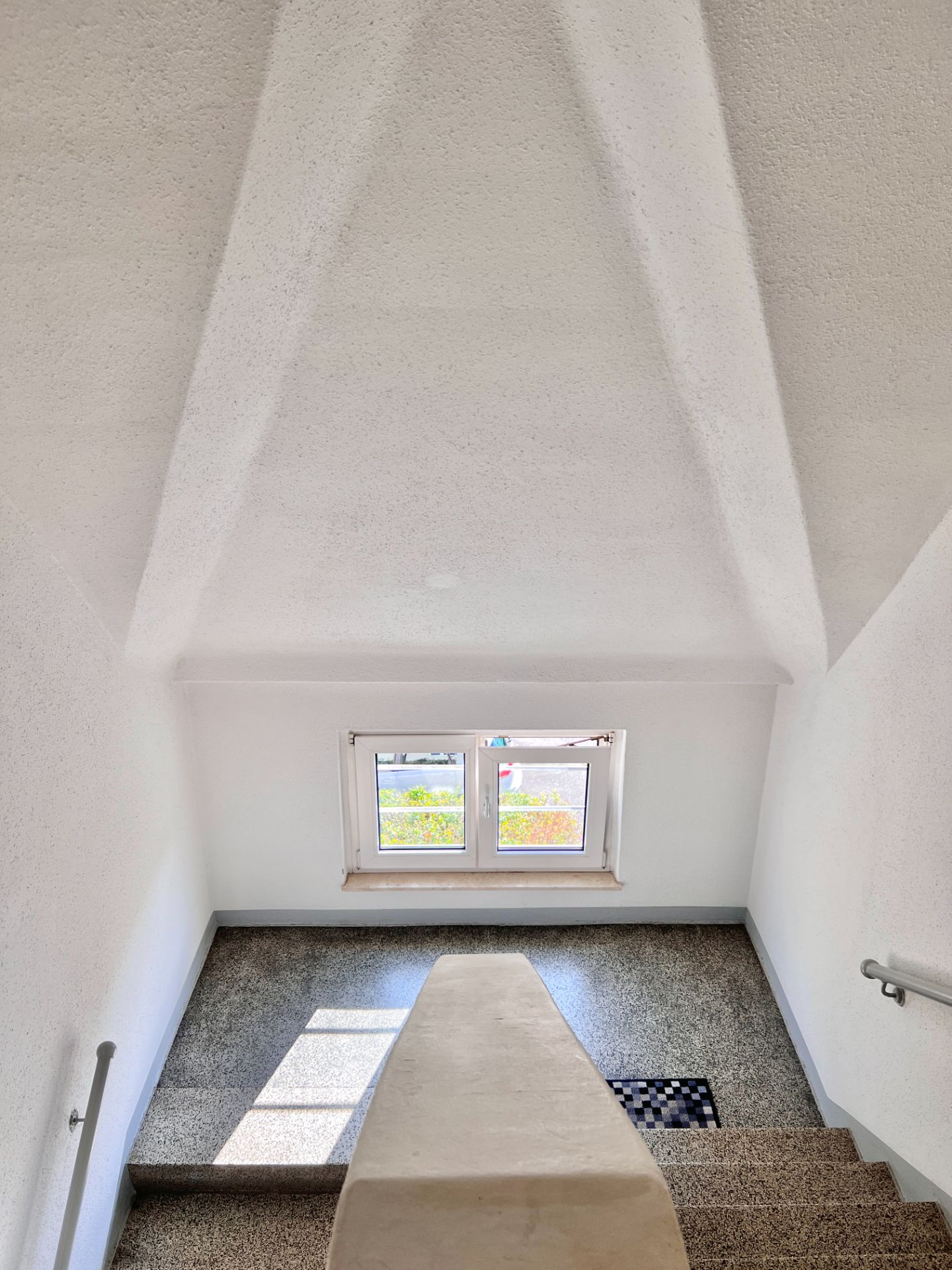 Helles Treppenhaus mit Fenster und Handläufen an beiden Seiten.