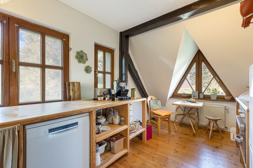 Helle Küche mit Holzfußboden, offenem Regal, Kaffeemaschine und kleinem Esstisch am Fenster.