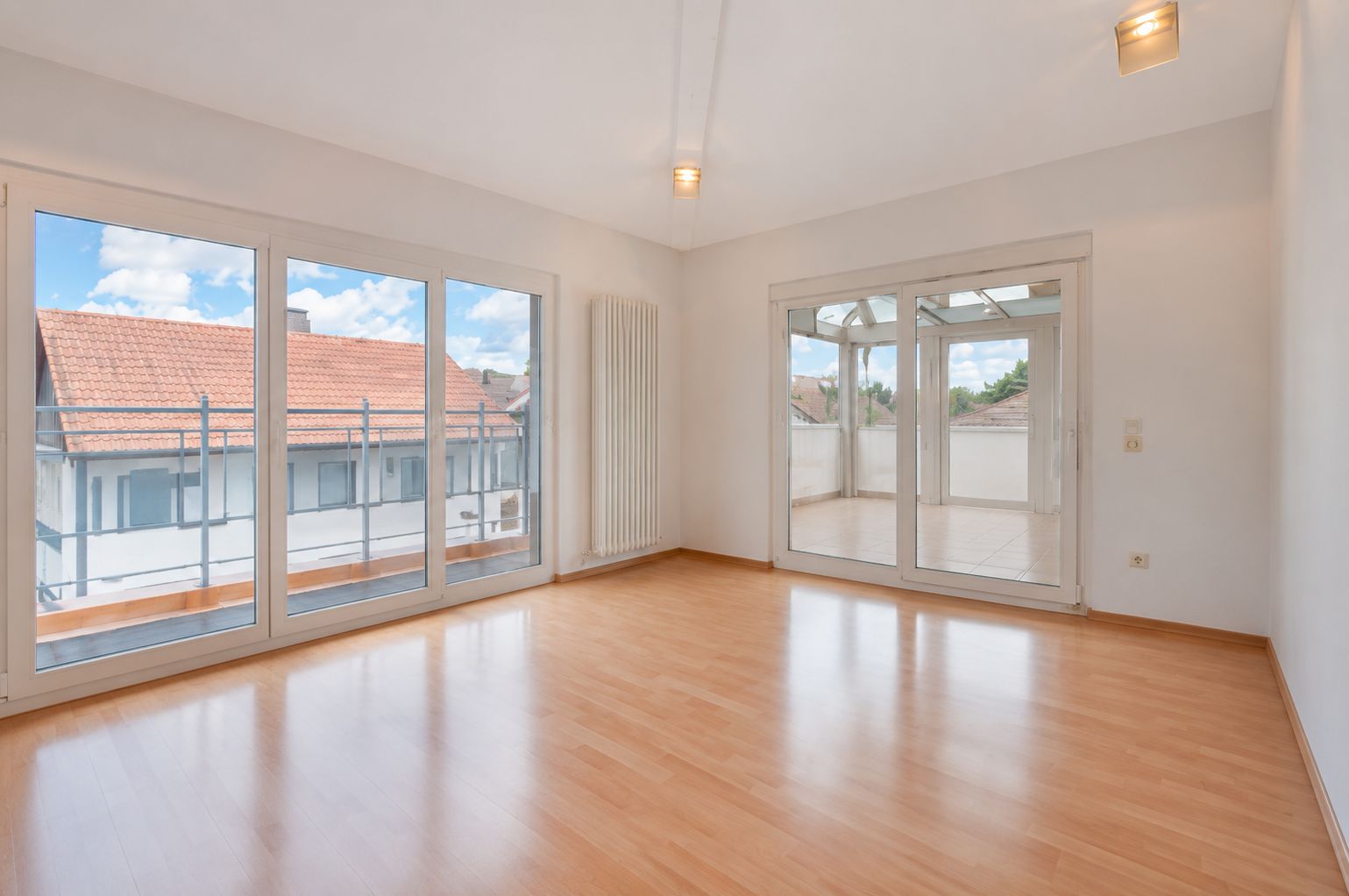 Heller Raum mit Parkettboden, großen Fenstern und Zugang zu einem Balkon oder Wintergarten.