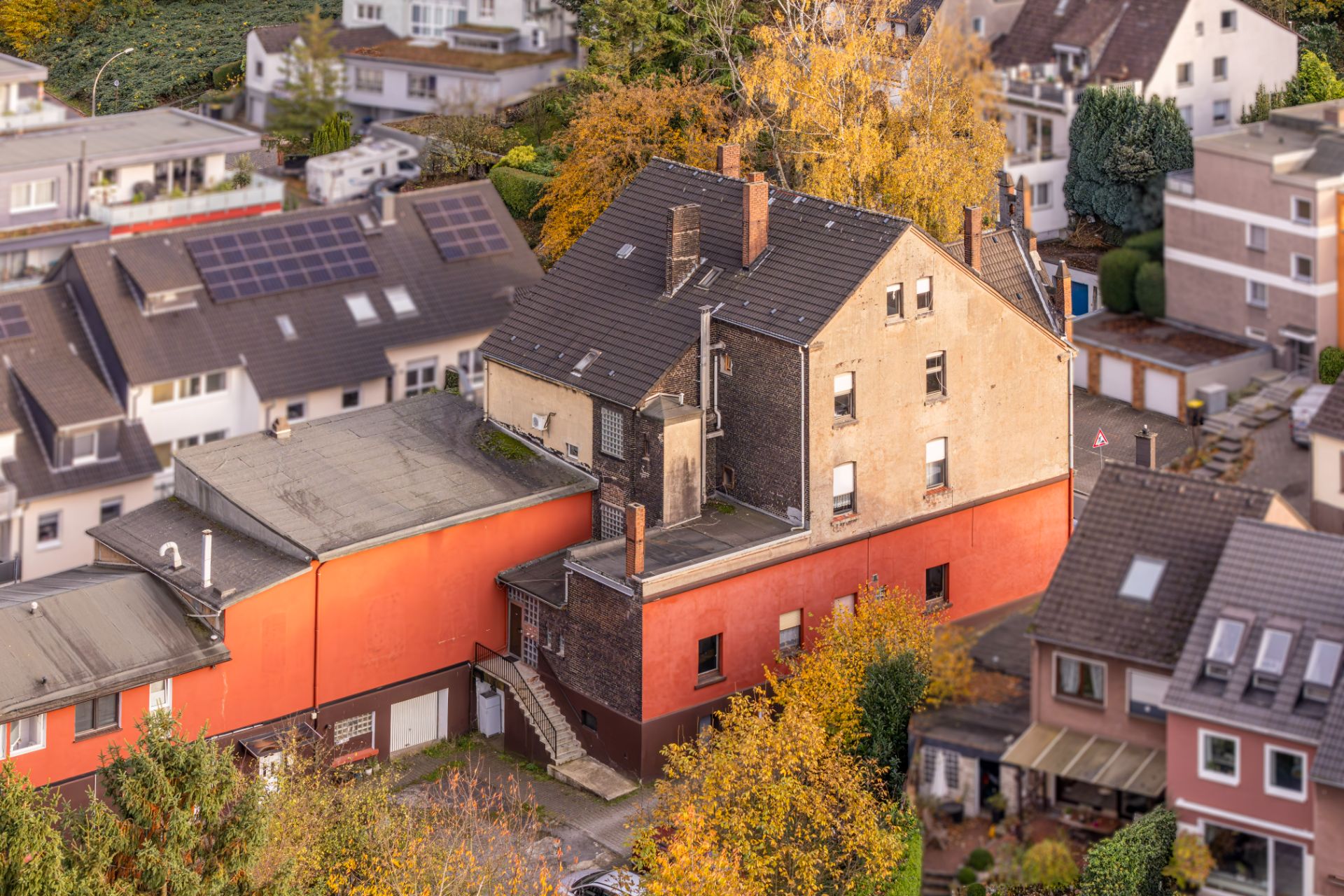 Mehrstöckiges Wohnhaus mit roter Fassade und Außentreppe, umgeben von weiteren Häusern und Bäumen.