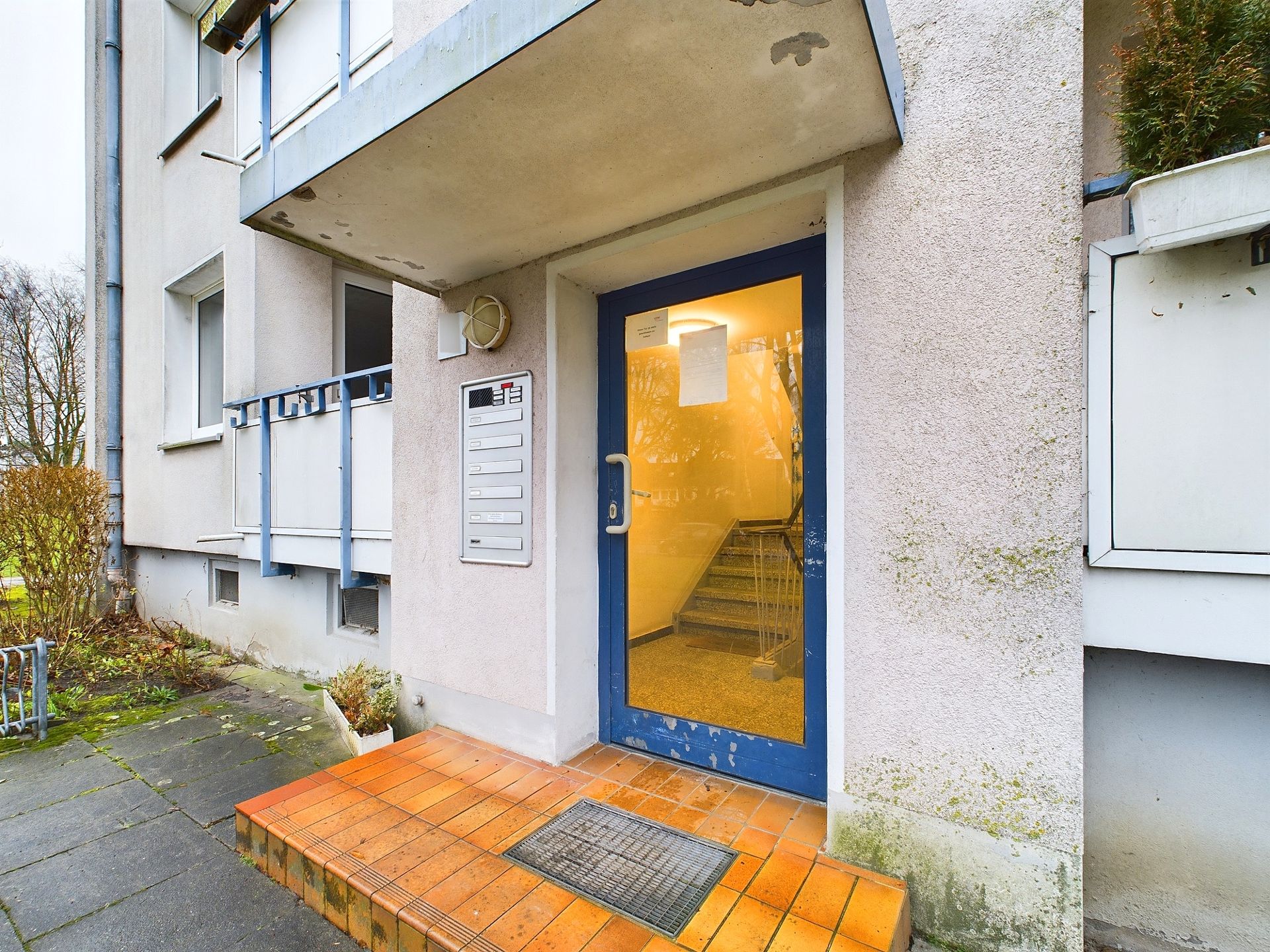 Eingang eines Mehrfamilienhauses mit blauer Tür und Briefkästen an der Wand.