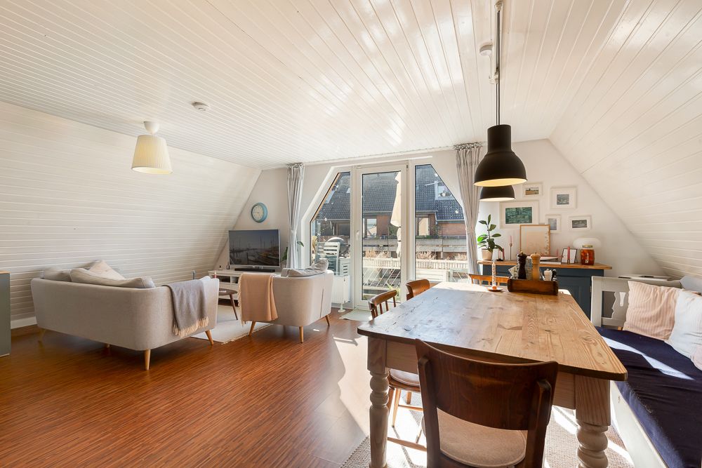 Helles Wohnzimmer mit Sofa, Esstisch und Zugang zu einem Balkon, Holzfußboden und weißen Wänden.