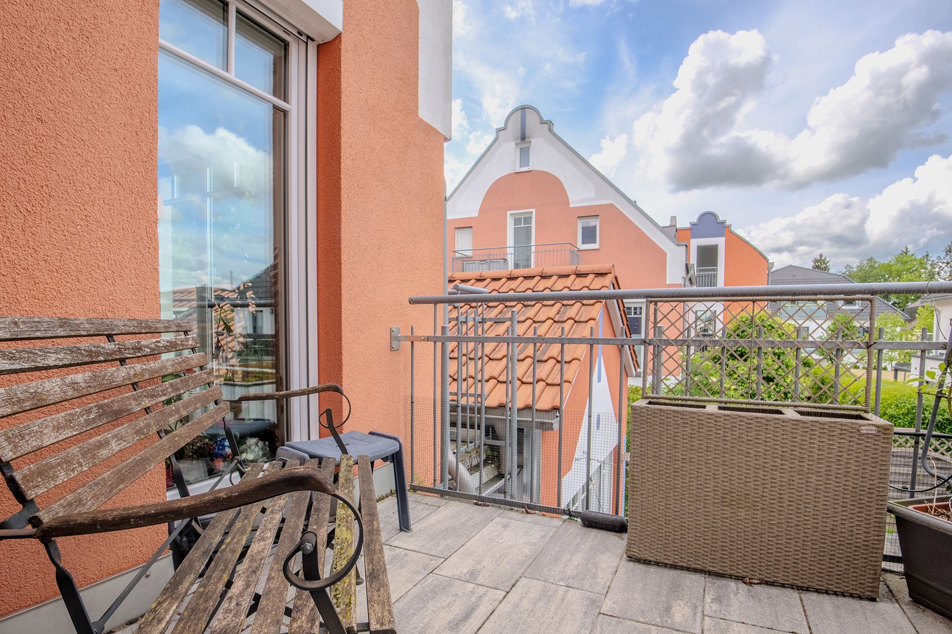 Kleiner Balkon mit Holzbänken, einem Hocker und Pflanzkasten, Blick auf Nachbarhäuser.