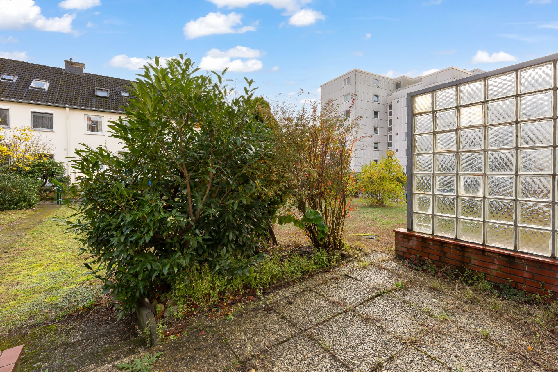 Garten mit Sträuchern und Glasbausteinwand auf Steinboden.