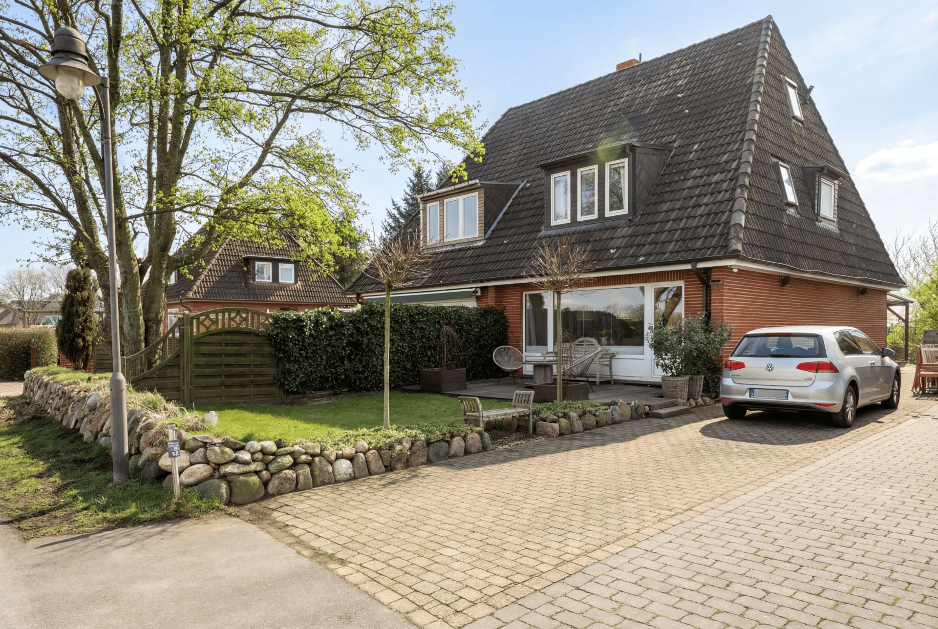 Zweistöckiges Einfamilienhaus mit schwarzem Dach, Einfahrt, Auto und Garten mit Bäumen.