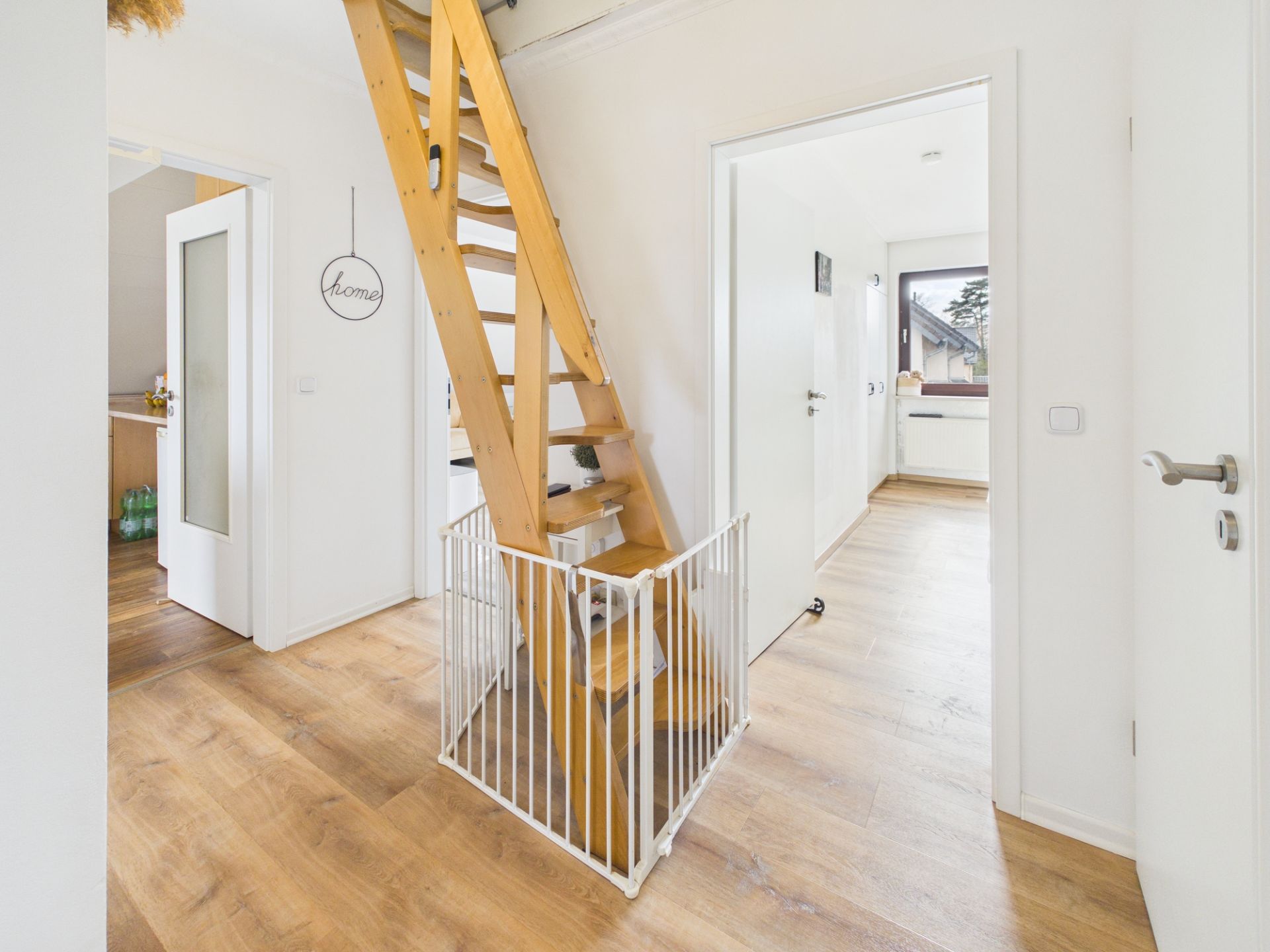Flur mit Holztreppe und Kinderschutzgitter, Türen zu weiteren Räumen, heller Holzboden.